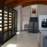 The rigid angles and dark metal trim of this modern wine cellar match beautifully with the curved wooden ceiling and open spaces in this home.